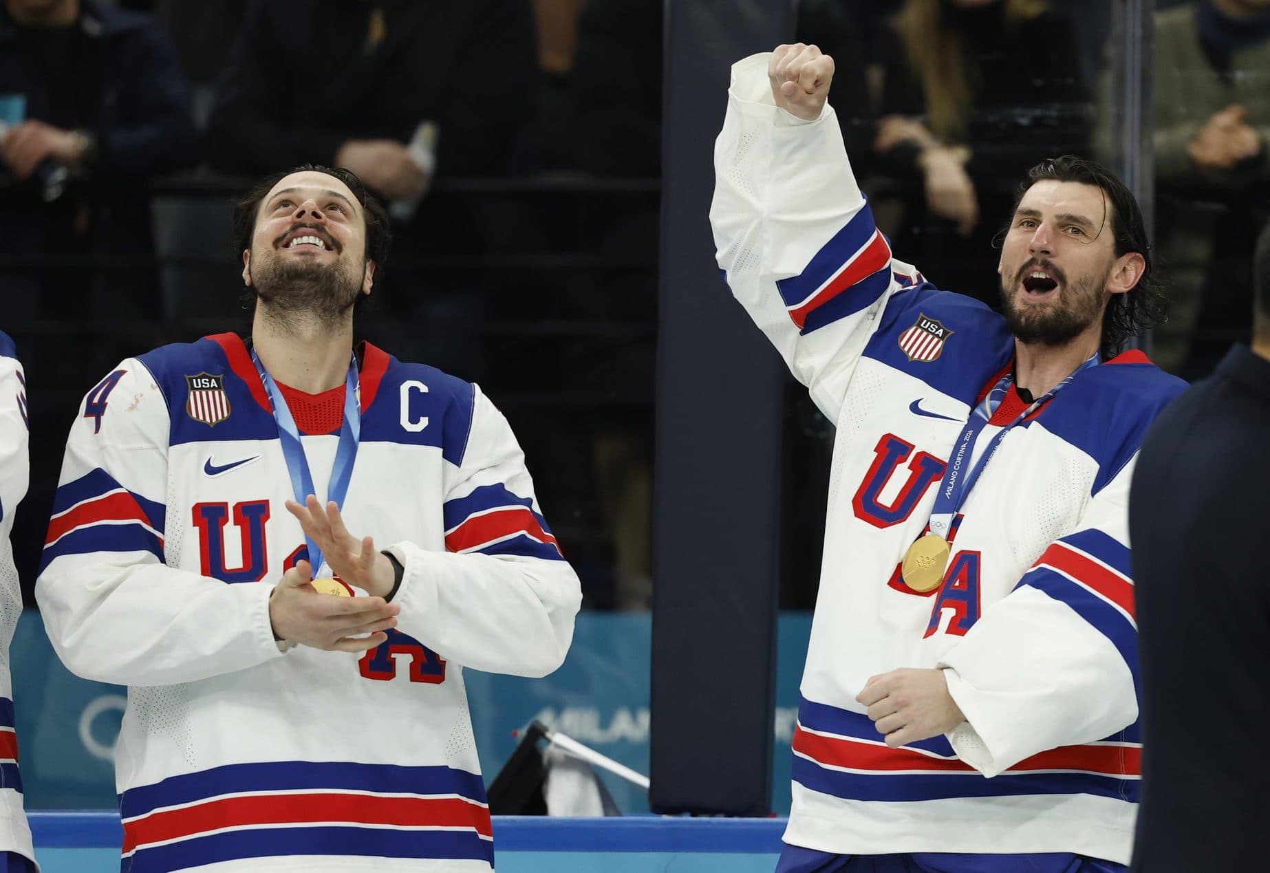 Auston Matthews (34) of the United States and Connor Hellebuyck (37) of the United States celebrate their gold medals against Canada in the men's ice hockey gold medal game during the Milano Cortina 2026 Olympic Winter Games at Milano Santagiulia Ice Hockey Arena.